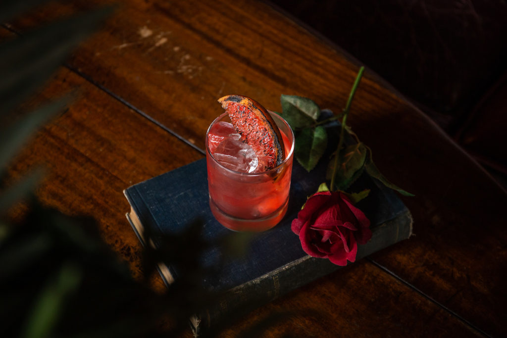 Cocktail on a book with a red rose next to it