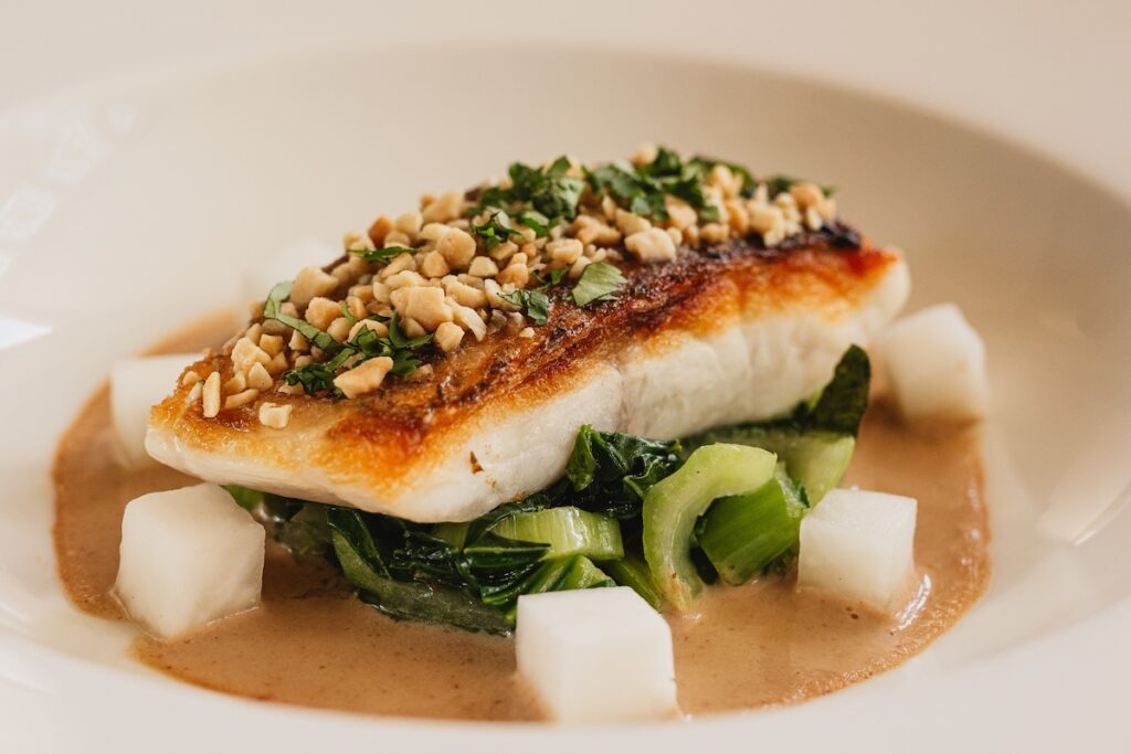 White fish on greens and brown sauce with nutty crust